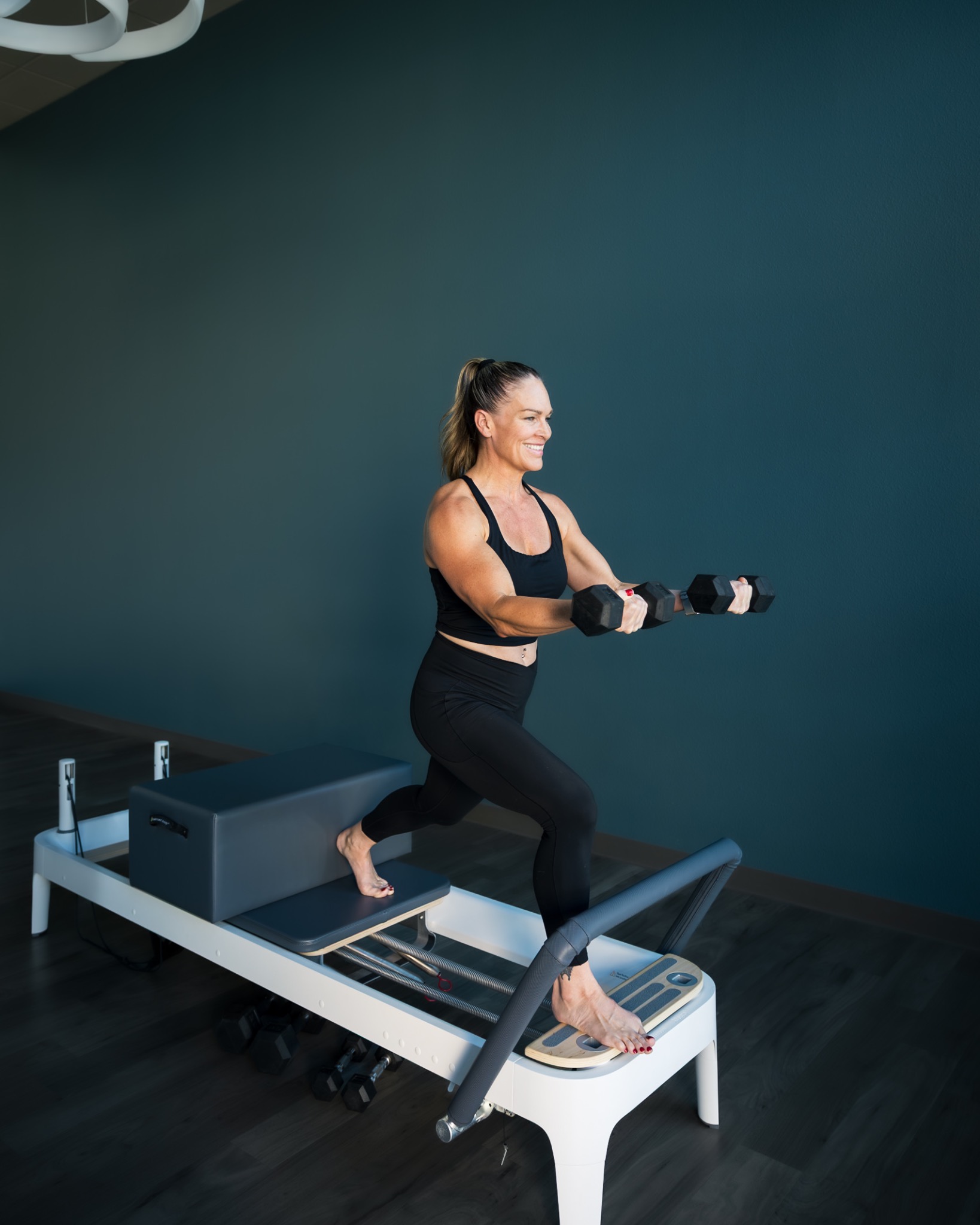 A woman holding dumbbells while lunging on a Pilates reformer